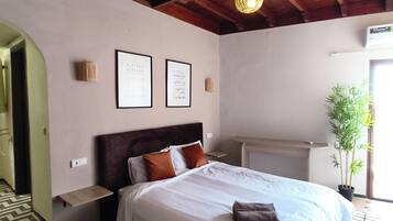 Un dormitorio con techo de madera, una cama con ropa de cama blanca, un tapete estampado y una planta en maceta.