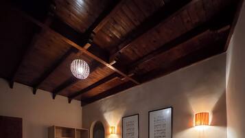 A bedroom with a large bed, wooden ceiling beams, a wardrobe, and wall-mounted sconces.