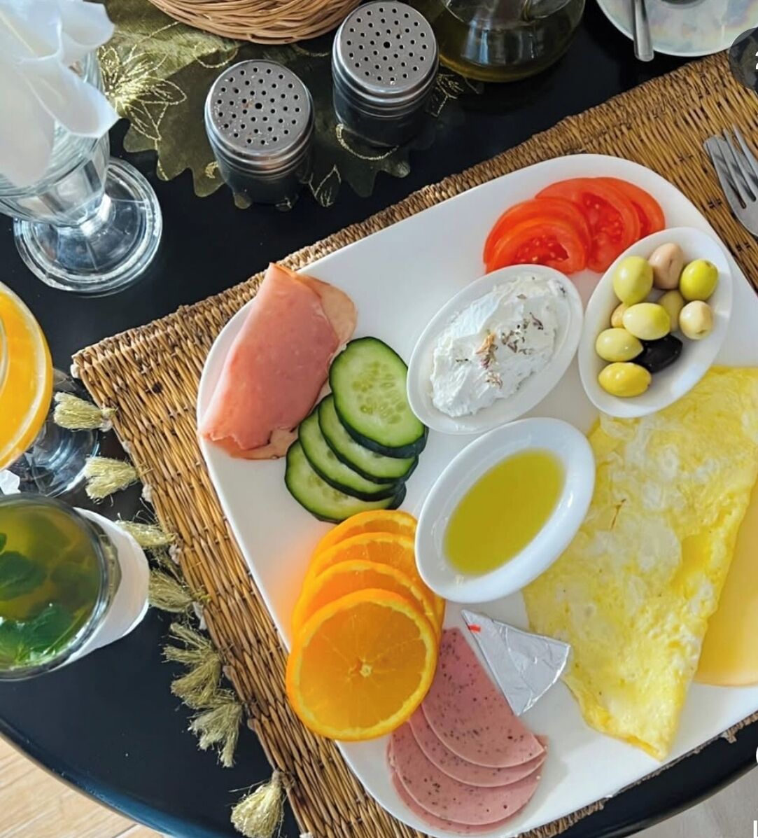 A breakfast plate with ham, cucumber slices, tomatoes, olives, yogurt, and an omelette.