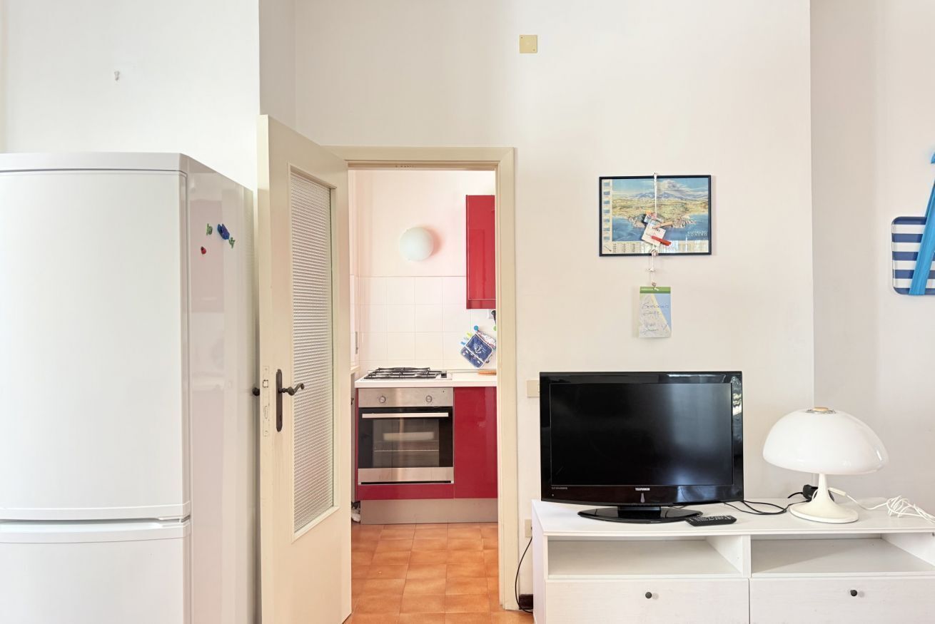 A compact kitchen with a refrigerator, oven, and a TV on a white cabinet.