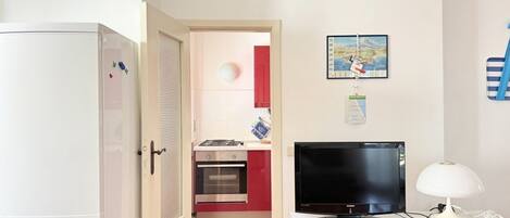 A compact kitchen with a refrigerator, oven, and a TV on a white cabinet.