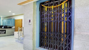 A hotel entrance with a metal gate, a reception desk, and a staircase leading to the interior.