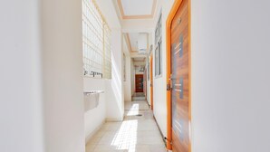 A narrow hallway with tiled flooring, a wooden door on the right, and a window with bars on the left.