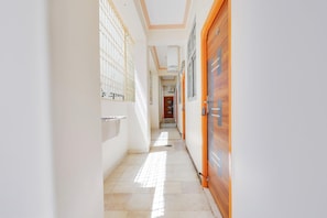 Un pasillo con suelo de baldosas, una puerta de madera a la derecha y una ventana con rejas a la izquierda.