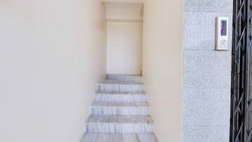Uma escadaria de mármore leva a um patamar com um painel de controle de elevador digital na parede.