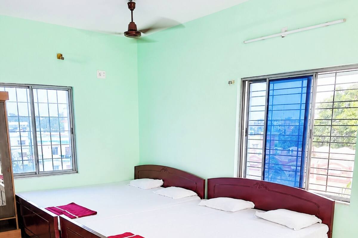 A bedroom with a large bed, two windows, a ceiling fan, and a door.