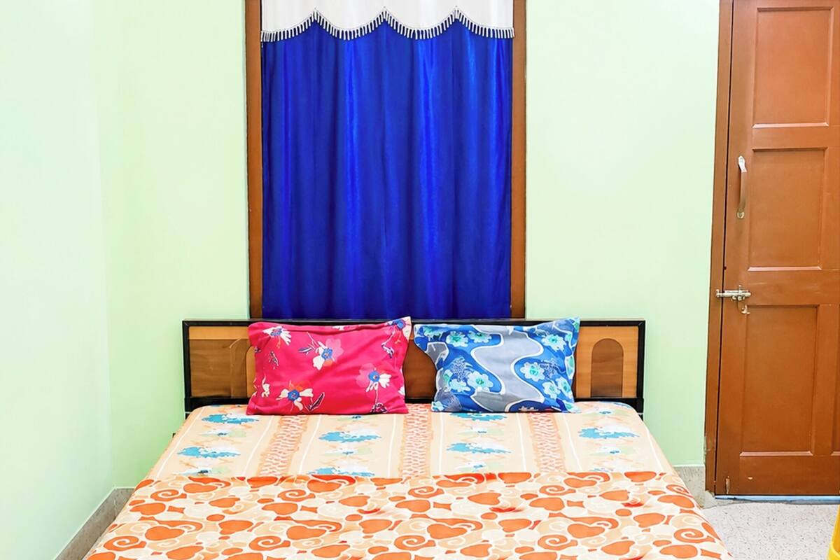 A bed with a patterned bedspread, two pillows, a blue curtain, and a wooden door.