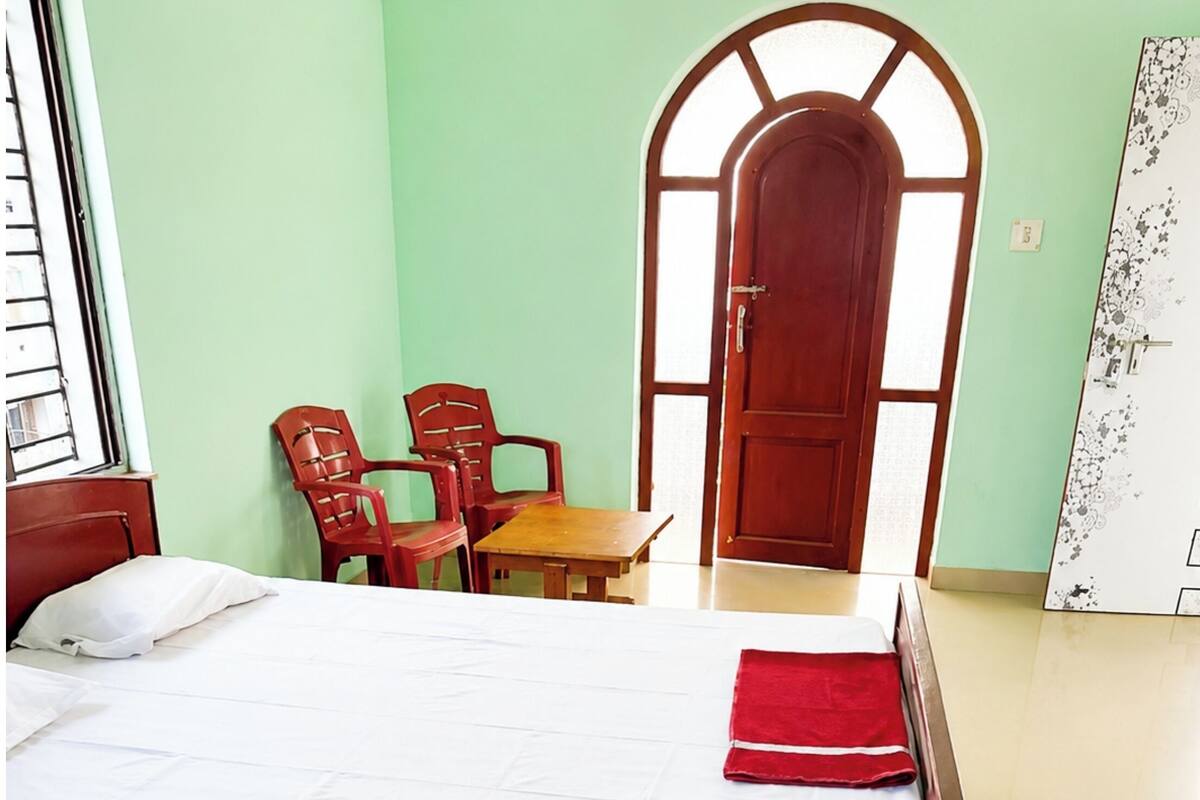 A hotel room with two beds, a wooden door, a small table, and two red chairs.