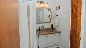 A bathroom with a white sink, a mirror with lights, a towel rack, and a wooden door.