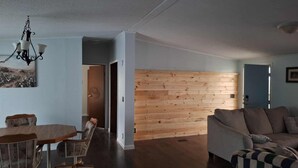A living room with a wooden wall, a dining area with a table and chairs, and a sofa. - Easy Access Ramp Entry  3-bedroom 2 bathroom Harrison Cottage with AC (Harrison)