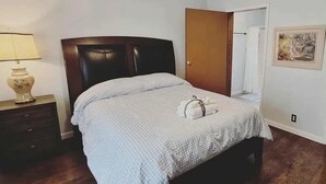 A bedroom with a bed, a nightstand, a lamp, a wooden floor, a door, and a framed picture on the wall. - Easy Access Ramp Entry  3-bedroom 2 bathroom Harrison Cottage with AC (Harrison)
