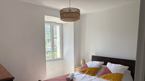 Un dormitorio con cama, mesita de noche, lámpara y ventana.