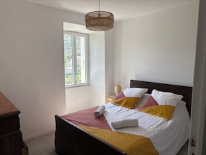 A bedroom with a bed, a bedside table, a lamp, and a window. - Quiet village house 10 minutes from the sea (Poggio)