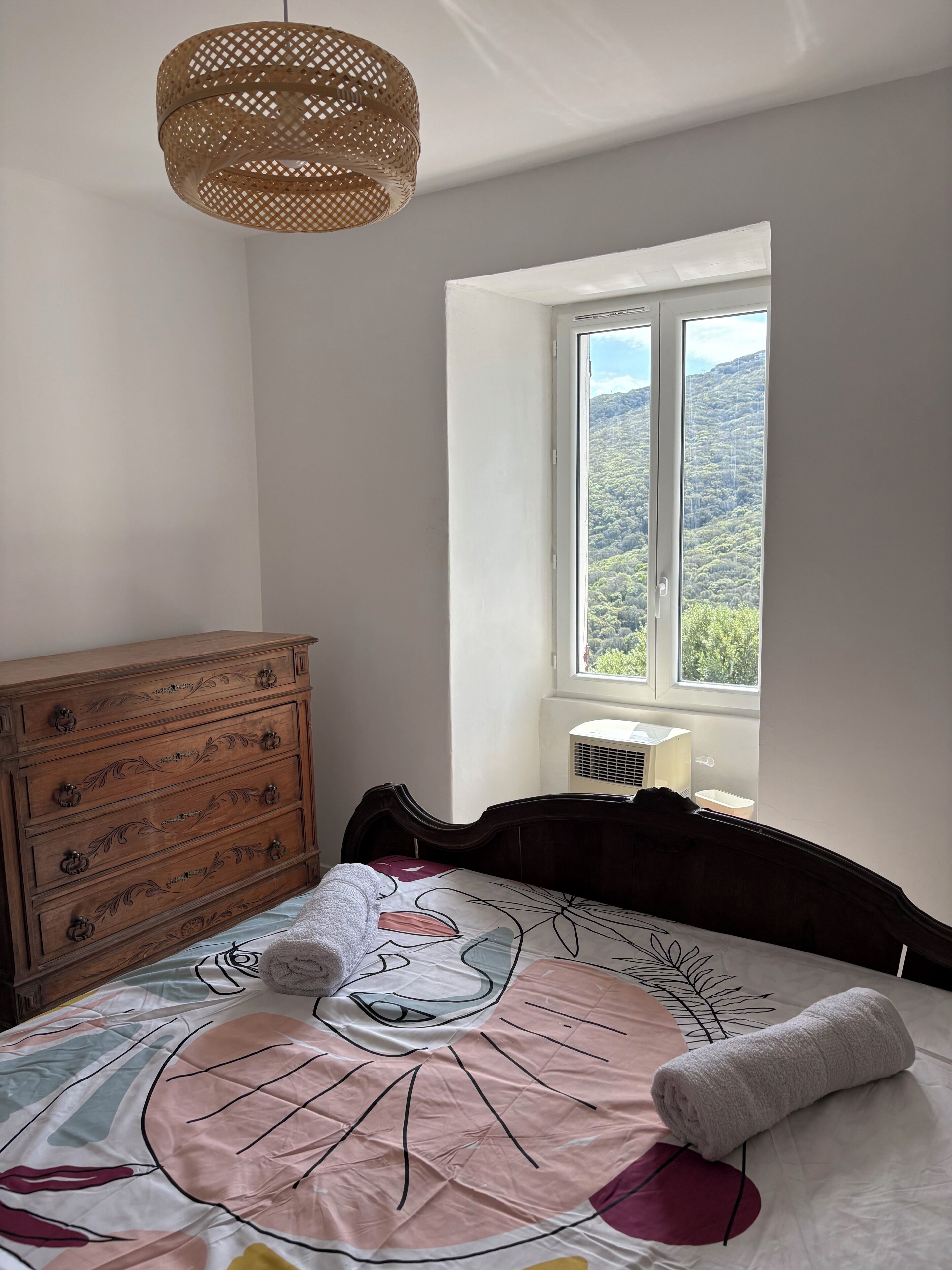 Une chambre à coucher avec un lit, une commode, une fenêtre donnant sur un beau paysage et un luminaire au plafond.