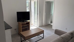 Un moderno salón con un televisor de pantalla plana sobre un soporte de madera, una mesa de centro de madera, un sofá color beige y una puerta corrediza de vidrio que da a un balcón.