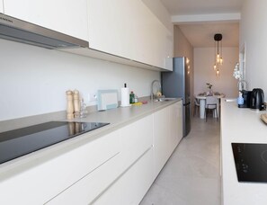 Eine moderne Küche mit weißen Schränken, einer schwarzen Induktionskochplatte, einem eingebauten Backofen und einem Edelstahlkühlschrank.