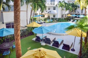 A pool area with lounge chairs and umbrellas, surrounded by palm trees and a building with balconies. - Charming 1BR Escape with Pool & Beach Nearby - (Key Biscayne)