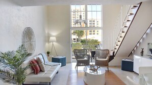 Ein geräumiges Wohnzimmer mit einem weißen Sofa, einem Couchtisch, Korbstühlen und Blick auf einen Balkon mit Gartenmöbeln.