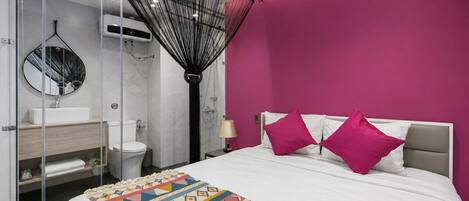 A modern bedroom with a bed, a bedside table, a nightstand, a large mirror, a bathroom with a toilet and sink, and a shower area.