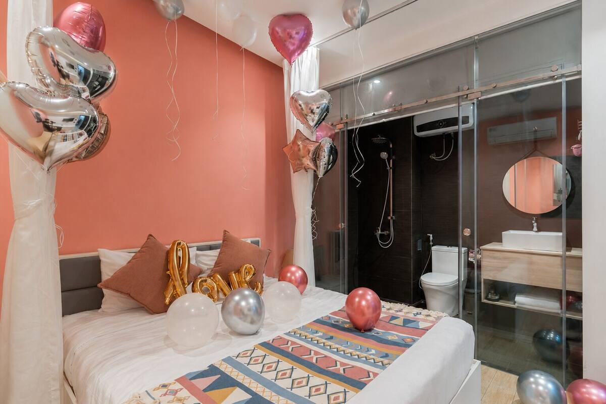 A bedroom with a bed, pillows, balloons, and a bathroom with a shower and toilet.