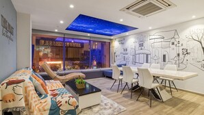 Una habitación de hotel moderna con sofá, una mesa de comedor con sillas, un tragaluz en el techo y un mural en la pared.