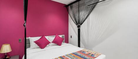 Una habitación de hotel con cama, mesita de noche, lámpara, mosquitero y aire acondicionado.