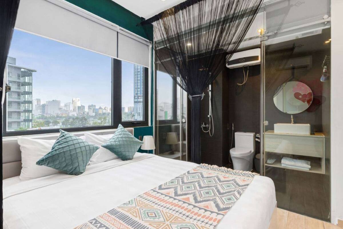 A modern hotel room with a large bed, a city view, a glass shower enclosure, and a vanity with a mirror.