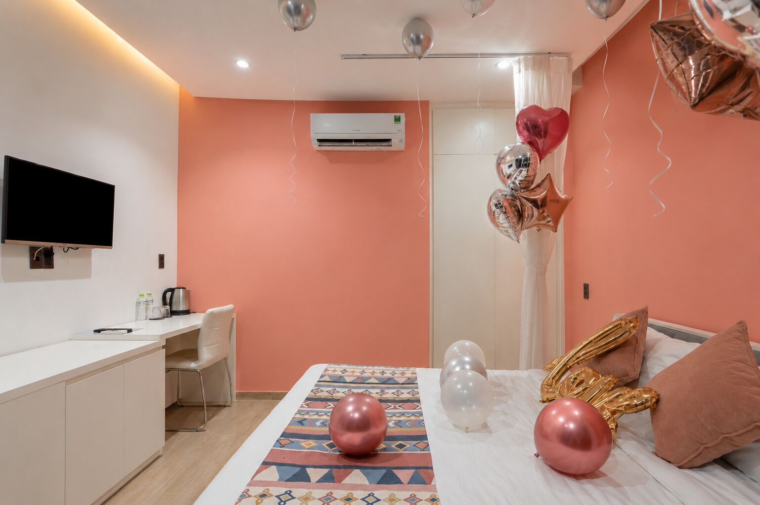 A modern hotel room with a bed, a desk, a flat-screen TV, and an air conditioning unit.