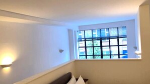 Una camera da letto con un letto, un comodino, una cassettiera, una finestra con persiane e una lampada a parete.
