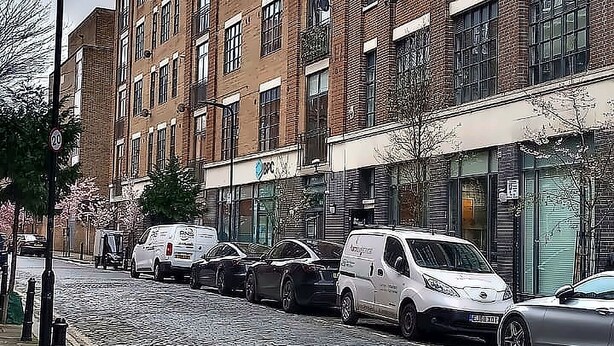 Un edificio in mattoni su più piani con una fila di auto parcheggiate su una strada acciottolata.