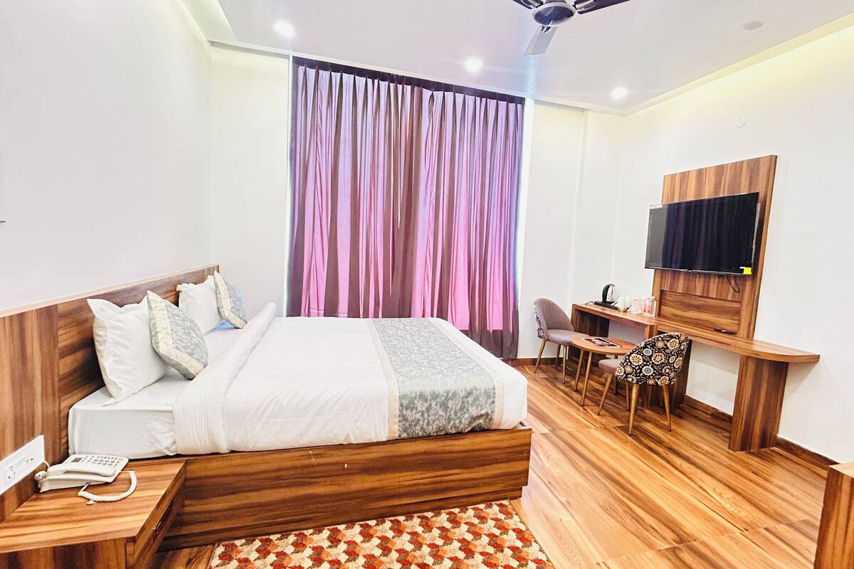 Une chambre à coucher moderne avec une tête de lit en bois, un lit recouvert de linge de maison blanc, un bureau avec une chaise, une télévision et un tapis à motifs.