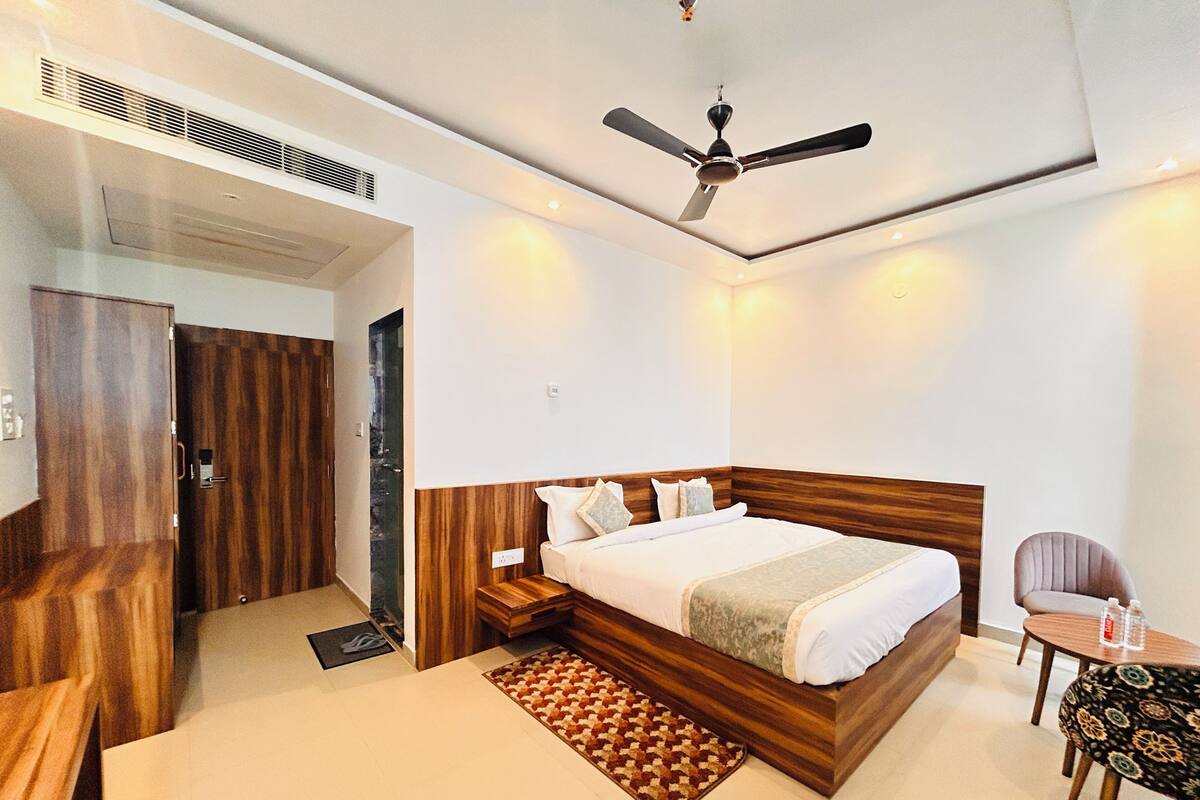 Une chambre d’hôtel moderne avec une tête de lit en bois, un lit simple, une petite table, une chaise et un ventilateur de plafond.