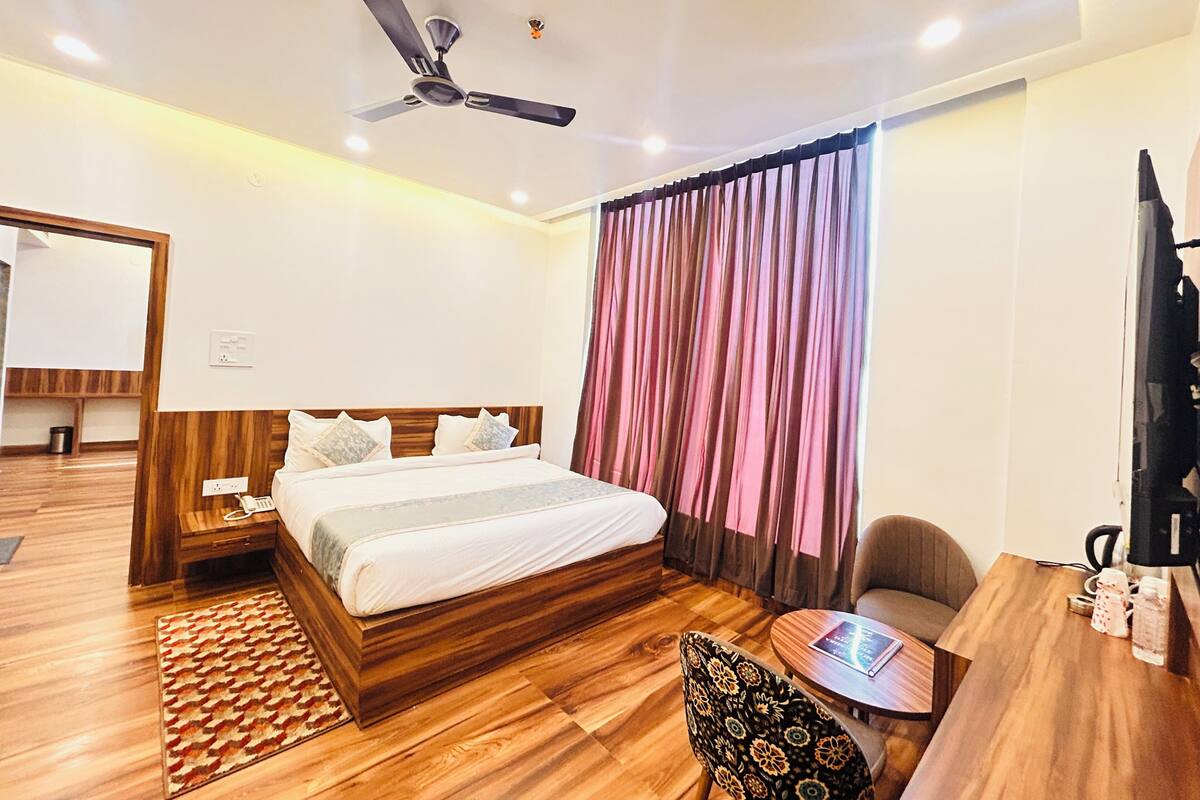 Une chambre d’hôtel équipée d’un lit, d’un bureau, d’une chaise, d’un ventilateur de plafond et d’une fenêtre avec des rideaux.