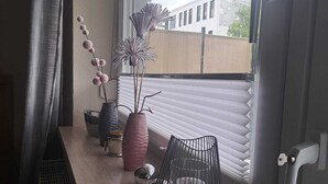 Un balcon avec une fenêtre, une chaise en métal et des objets décoratifs, notamment des vases et une plante.