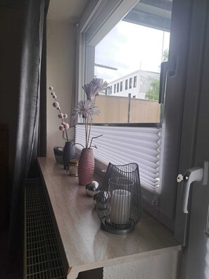 Ein Balkon mit Fenster, einem Metallstuhl und Dekorationselementen wie Vasen und einer Pflanze.