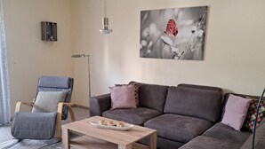 Un salon avec un canapé gris, une table basse en bois, un lampadaire et un tableau représentant une fleur accroché au mur.