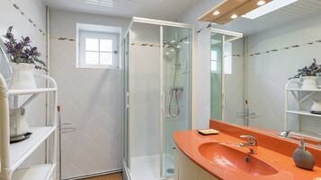 A modern bathroom with a glass-enclosed shower, a vanity with an orange sink, and a large mirror.