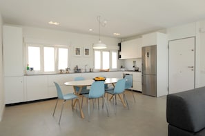 A modern kitchen with white cabinets, a stainless steel refrigerator, a dining table with blue chairs, and a hanging pendant light. - San José, first line sea view - sea front (San José)