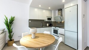 A modern kitchen with white cabinets, a round wooden table, and white chairs. - Modern apartment, Montgó views, pool & private parking near Dénia centre & beach (Dénia)