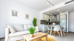 A modern living room with a sofa, a coffee table, and a dining area with chairs and a table. - Modern apartment, Montgó views, pool & private parking near Dénia centre & beach (Dénia)