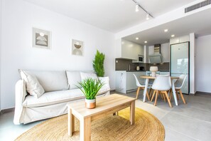 A modern living room with a sofa, a coffee table, and a dining area with chairs and a table. - Modern apartment, Montgó views, pool & private parking near Dénia centre & beach (Dénia)