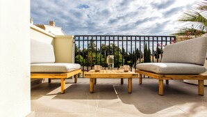 A terrace with two sofas and a wooden table, a metal fence, and a view of trees and buildings. - Modern apartment, Montgó views, pool & private parking near Dénia centre & beach (Dénia)