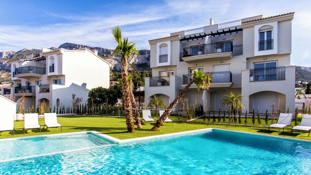 A swimming pool with lounge chairs, a well-maintained lawn, and a multi-story building with balconies. - Modern apartment, Montgó views, pool & private parking near Dénia centre & beach (Dénia)