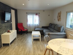 Un salon moderne avec un canapé, un fauteuil rouge, une table blanche et un téléviseur fixé au mur en briques.