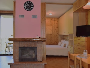 Een kamer met een open haard, een bed, een televisie en een klok aan de muur.