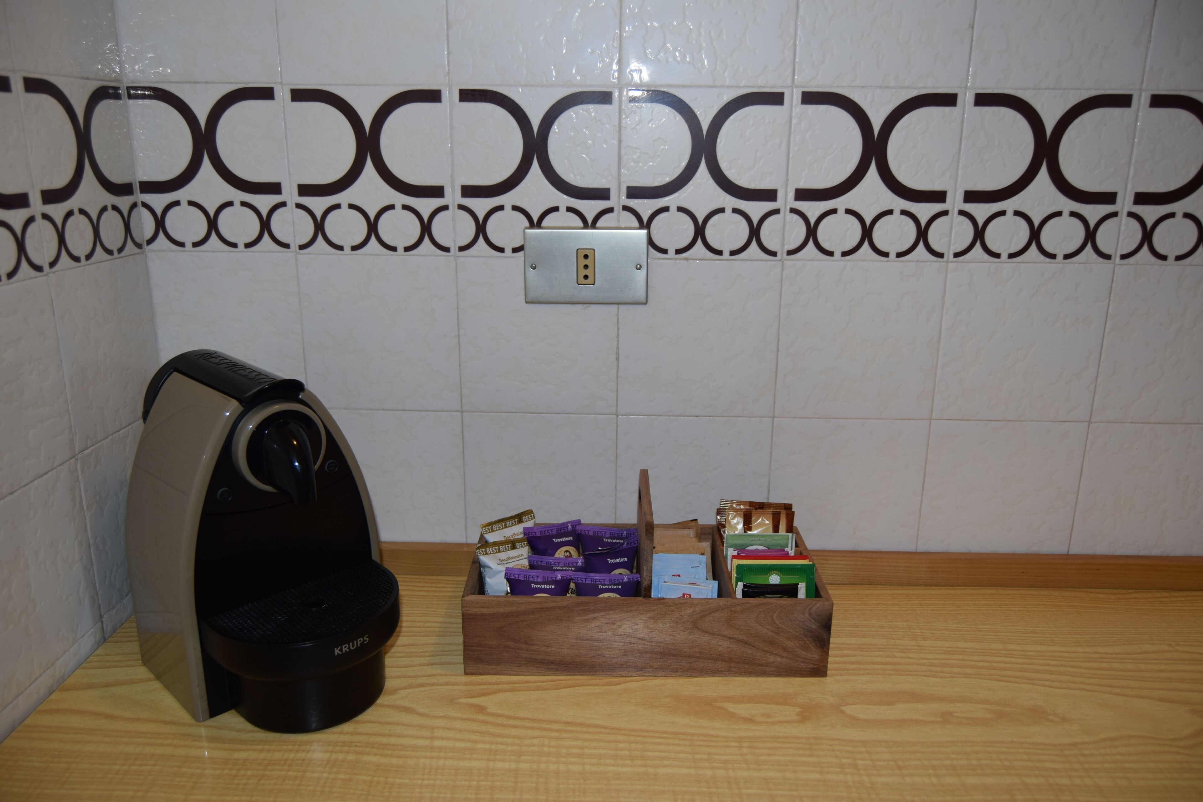Een koffieapparaat, een houten doos met verschillende voorwerpen, en een muur met een decoratief patroon.