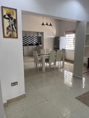 A modern kitchen with checkered backsplash, a dining area with a white table and chairs, and a painting on the wall. - Havillah Court. Cosy Hill Top Residence. AC. WIFI. Solar. (Freetown)