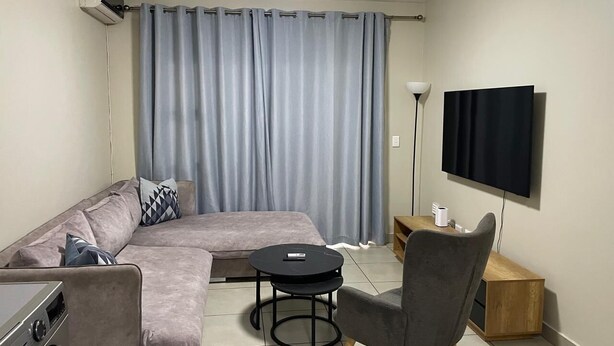 A living room with a sofa, a round coffee table, a TV, and a lamp. - Rivonia Modern 2Bed Apartment (Sandton)