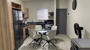 A compact kitchen with a refrigerator, microwave, stove, and dining table with chairs. - Rivonia Modern 2Bed Apartment (Sandton)