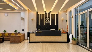 A reception desk with a 'JB SQUARE' logo, a clock, and a reception area with a sofa and potted plants. - Hotel JB Square Ayodhya Near Ram Mandir, Airport & Ayodhya Cantt (Faizabad)